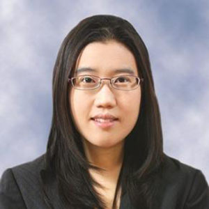 A woman with dark hair to her shoulders and eyeglasses gazes at the camera.