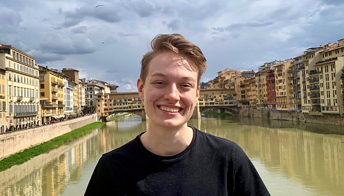 A person in a black tee shirt stands in front of a picturesque canal.