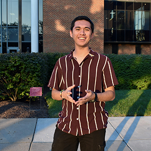 A young man in a brown shirt with white stripes smiles broadly.