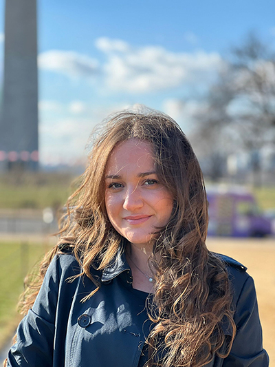  A young woman with long brown hair smiles and stands in front of the Washington Monument.