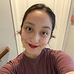 A young woman wearing a maroon shirt sits and smiles at the camera