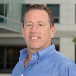 A man in a blue shirt smiles at the camera.