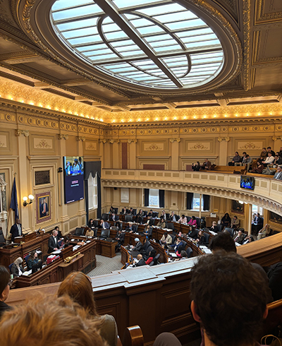 From a balcony, a group of students watch legislators working below in an ornately decorated room.