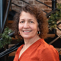 A woman in an orange shirt stands outside and smiles